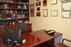 A shiny brown desk in front of a bookshelf filled with objects in the Donahue Building for Donahue & Associates LLC in Grafton, WI.